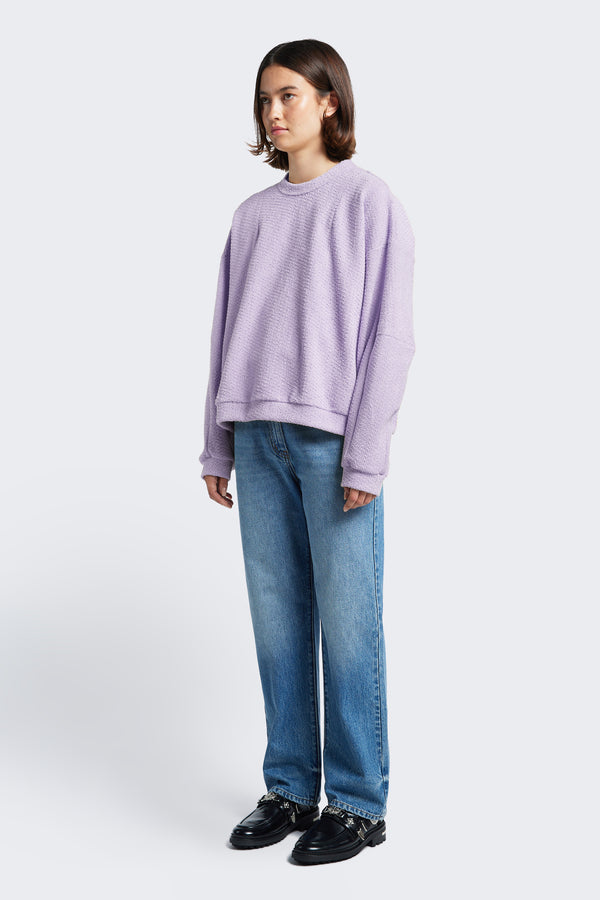 The Respite Sweater is a cropped jumper with a relaxed silhouette and features panelled sleeves and front darts in the collars. The loop front jersey in Lilac brings visual interest.