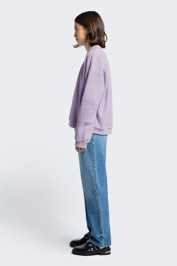 Side profile of Respite Sweater Lilac Purple, a cropped style jumper with a relaxed silhouette and panelled sleeves.