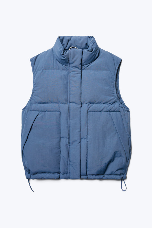 The front of the Stay Quilted Puffer Vest Blue, is a quilted down vest with high neckline, centre zip and press stud closure, elasticated armholes, side pockets and elastic waist pulls with toggles.