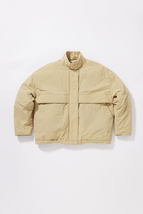 Flat Front of the sand beige Surge Quilted Jacket worn closed, showing relaxed silhouette, military tab collar and storm flap pocket detailing