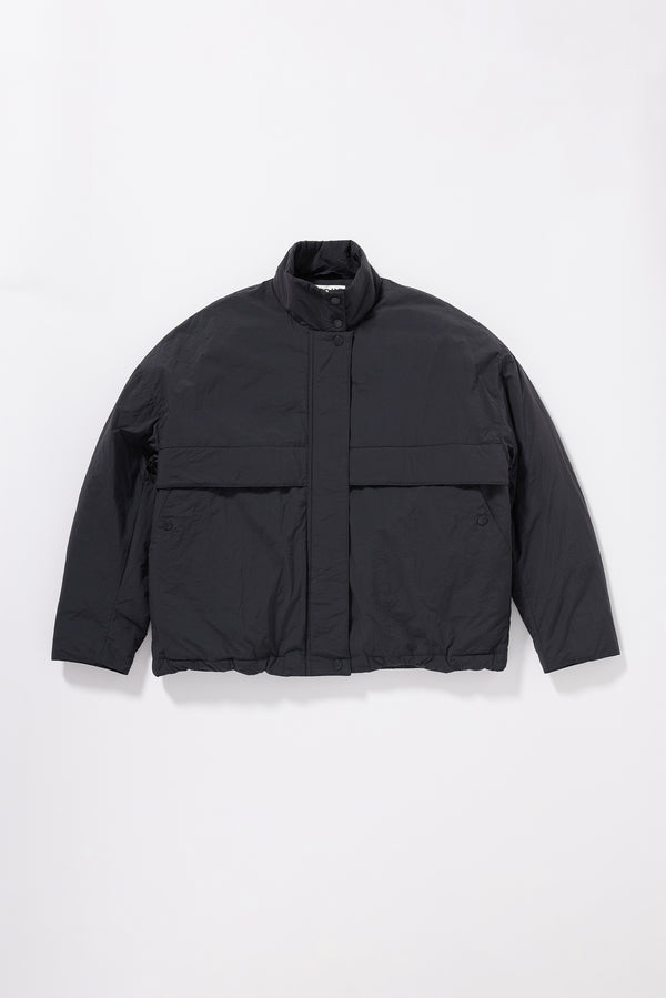 Flat Front of the black Surge Quilted Jacket worn closed, showing relaxed silhouette, military tab collar and storm flap pocket detailing