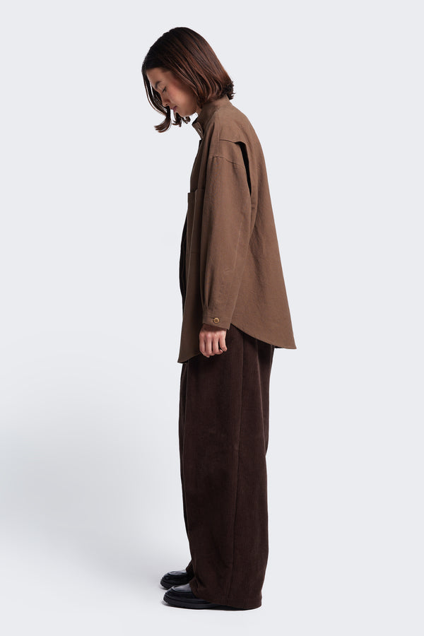 Side profile of the Tenet Blouson Shirt Brown, a long sleeve shirt with a high stand collar with button closure and back vent details. 