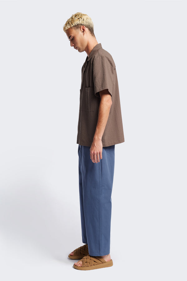 Side of The Boulder Pleat Pants in Blue, crafted from cotton herringbone twill, featuring side slant pockets, back patch pockets, and an elastic waistband with internal pull. Available in 5 sizes. 