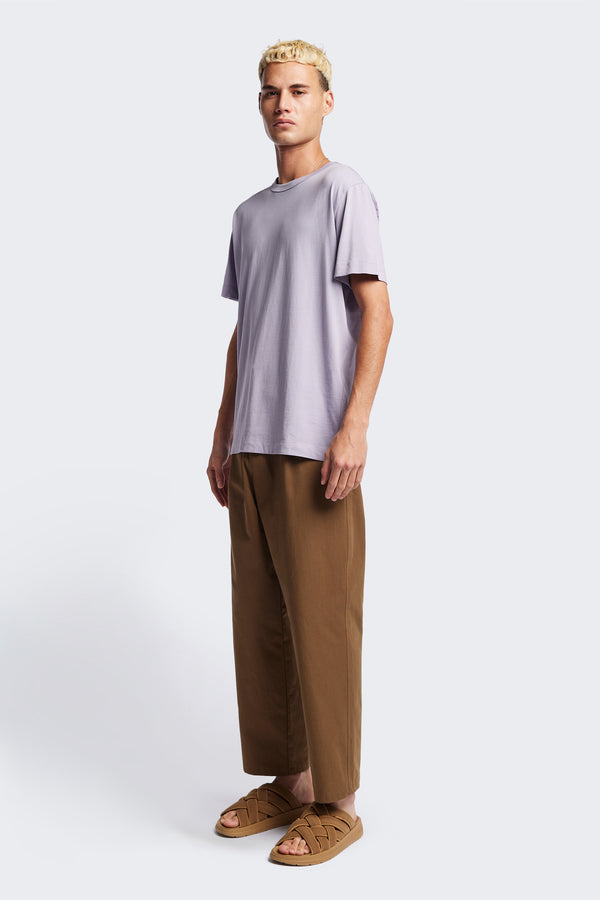 The Boulder Pleat Pants in Brown, crafted from cotton herringbone twill, featuring side slant pockets, back patch pockets, and an elastic waistband with internal pull. Available in 5 sizes. 