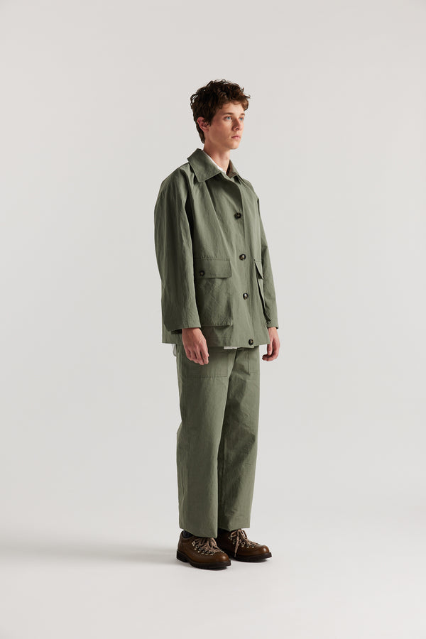 Front angle view of male model in Olive Lenz Pant with straight-leg silhouette, front patch pockets and twin-needle topstitch detail.