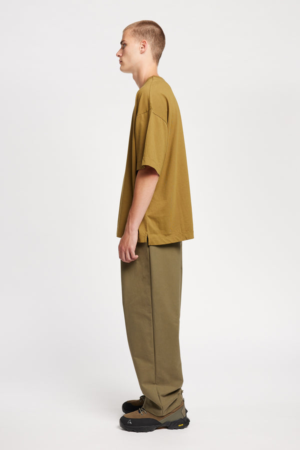 Side view of model wearing the logic pleat pant in Olive. A relaxed cotton trouser with pleated front and tapered leg