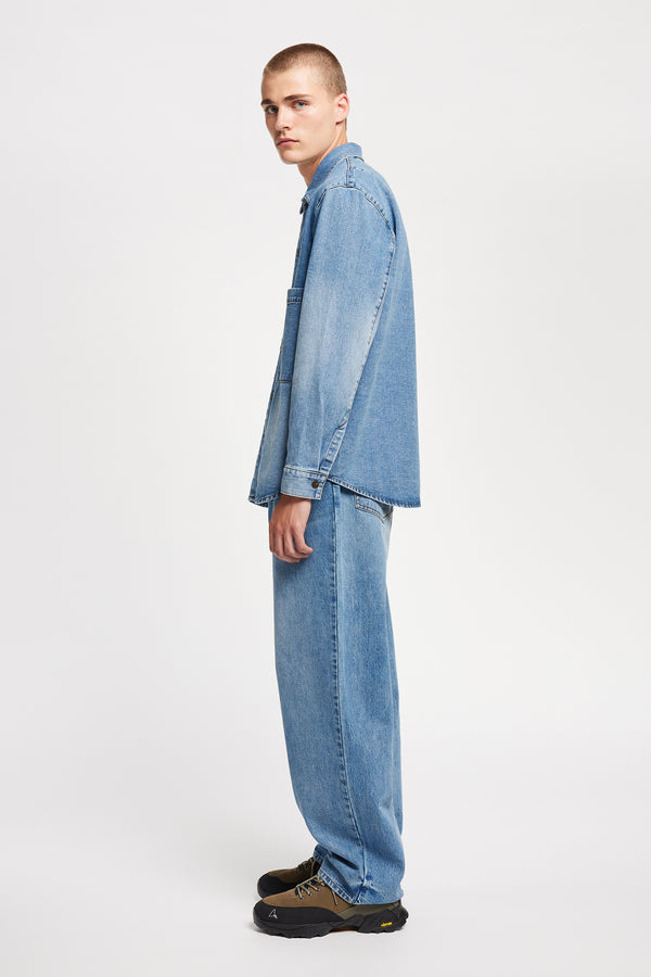 Side view of model wearing the Mascot relaxed fit denim shirt in mid-blue, featuring utility chest pockets.