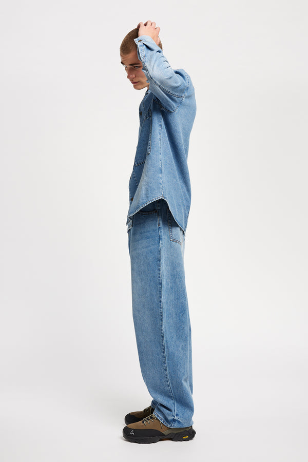 Side view of model wearing the Mascot relaxed fit denim shirt in mid-blue, featuring utility chest pockets.