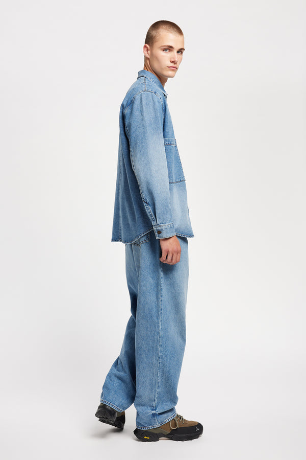 Side view of model wearing the Mascot relaxed fit denim shirt in mid-blue, featuring utility chest pockets.