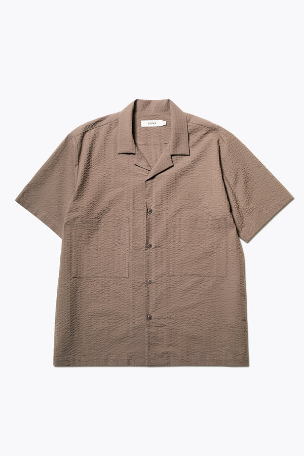 The Mirari Shirt in Brown, a relaxed short-sleeve camp shirt in soft textured cotton seersucker with an open collar and laid-back fit, styled for versatile wear. Available in 5 sizes. 