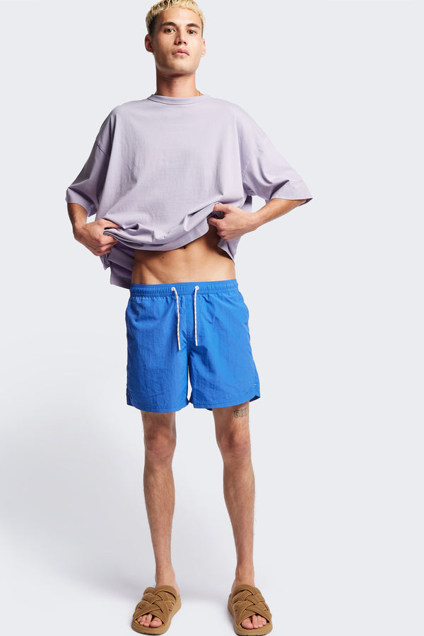 The New Wave Short in Lapis Blue. Swim shorts with elastic drawstring waist, internal mesh support, and front slant pockets. Available in 5 sizes.