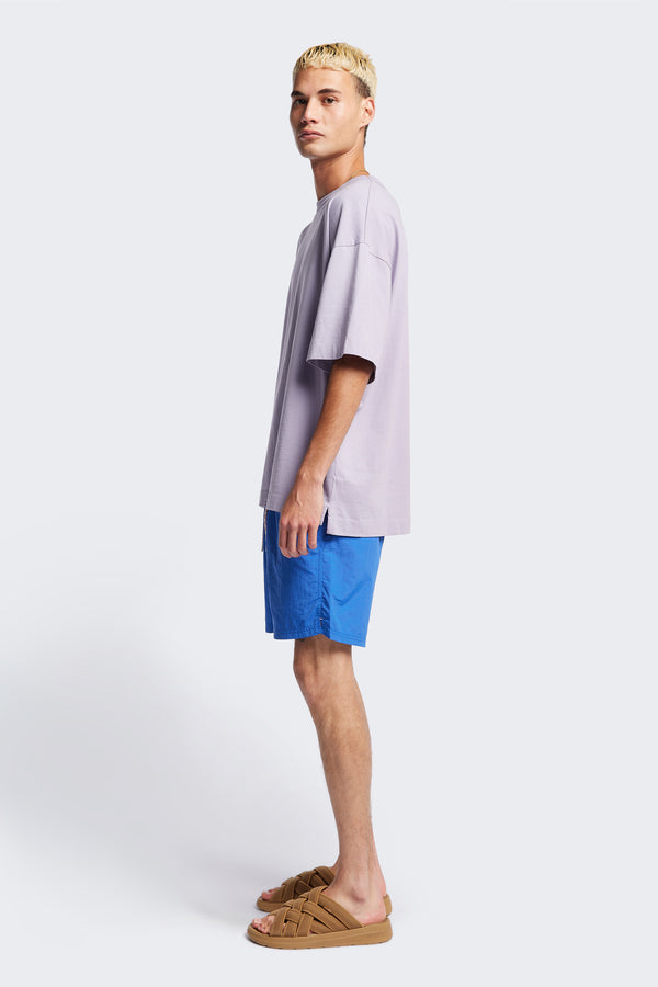 Side of The New Wave Short in Lapis Blue. Swim shorts with elastic drawstring waist, internal mesh support, and front slant pockets. Available in 5 sizes.