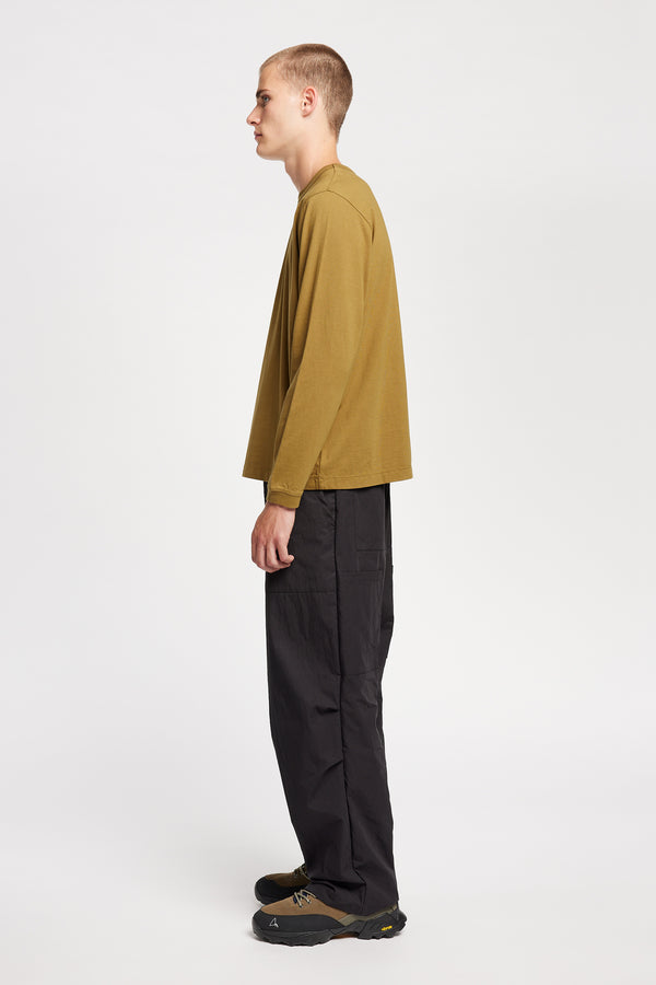 Side view of model wearing Output Pant in black, a relaxed fit with wide tapered leg and clean patch pockets 