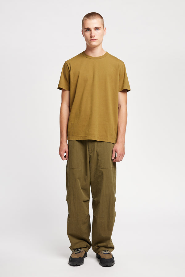 Front view of model wearing Output Pant in kelp green, a relaxed fit with wide tapered leg and clean patch pockets 
