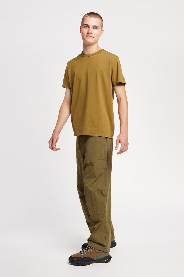Side view of model wearing Output Pant in kelp green, a relaxed fit with wide tapered leg and clean patch pockets 