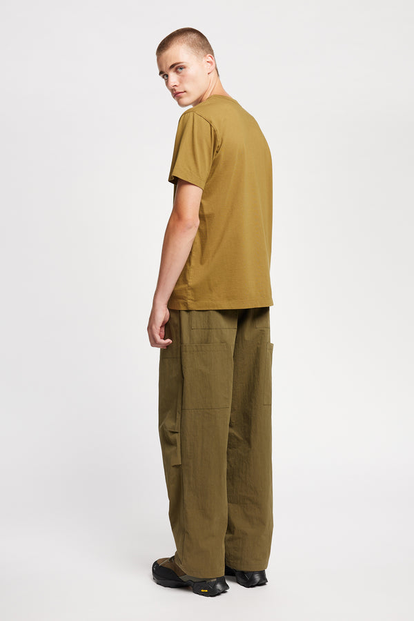 Back view of model wearing Output Pant in kelp green, a relaxed fit with wide tapered leg and clean patch pockets 