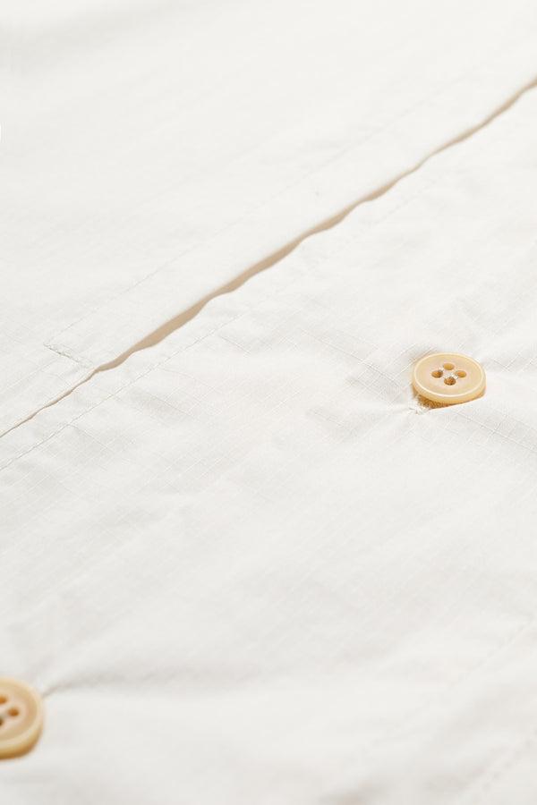 Close up of the Ecru Perisi shirt in lightweight micro ripstop cotton, featuring deep double patch map pockets at the chest, buttoned-up design, and a relaxed straight hemline. Available in sizes XS, S, M, L, and XL.