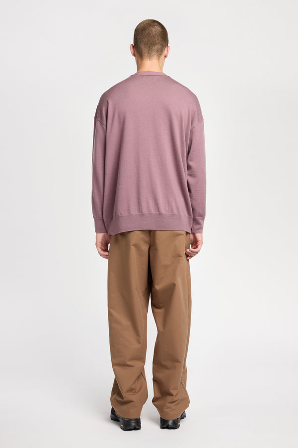 Back of Model wearing loose fit merino wool crew neck sweater with exposed seams in mauve. 