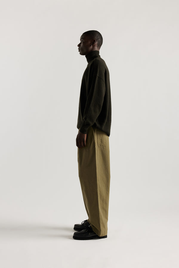 Side view of male Model wearing mock neck merino wool fisherman sweater with exposed seams in Darkest Green. 