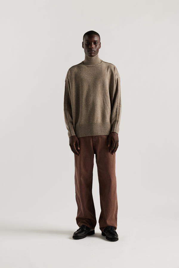 Front of Model wearing mock neck merino wool fisherman sweater with exposed seams in Taupe. 