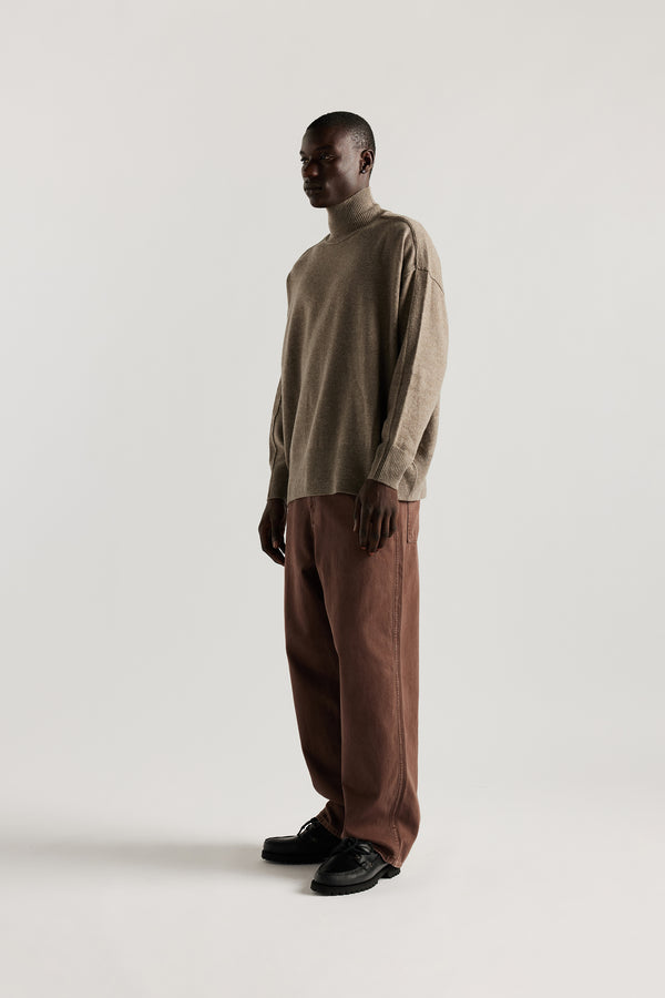 Front angle of male Model wearing mock neck merino wool fisherman sweater with exposed seams in Taupe. 