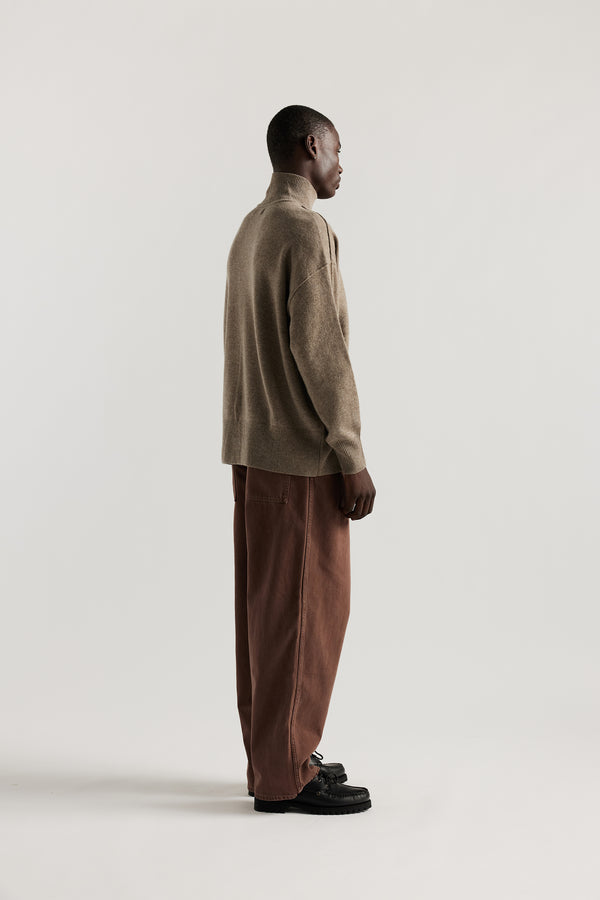 Back Angle of Model wearing mock neck merino wool fisherman sweater with exposed seams in Taupe. 