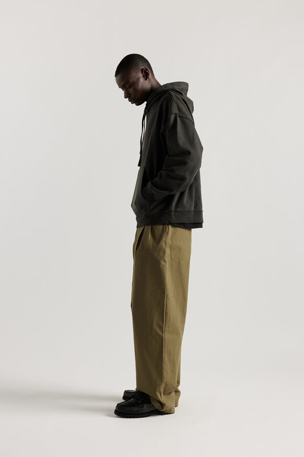 Side of model wearing oversized pigment-dyed hoodie with dropped shoulders and kangaroo pocket in jet black