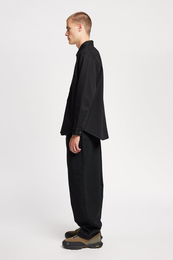 Side view of model in the renew jean, a relaxed loose-fit straight style in premium Japanese denim, shown in black with five-pocket design and custom branded hardware.
