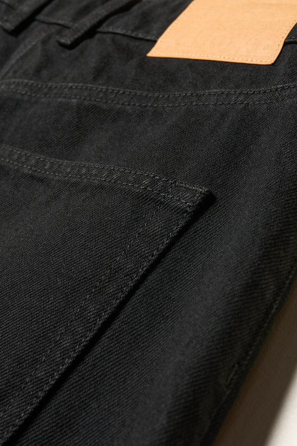 Close up of the renew jean, a relaxed loose-fit straight style in premium Japanese denim, shown in black with five-pocket design and custom branded hardware.