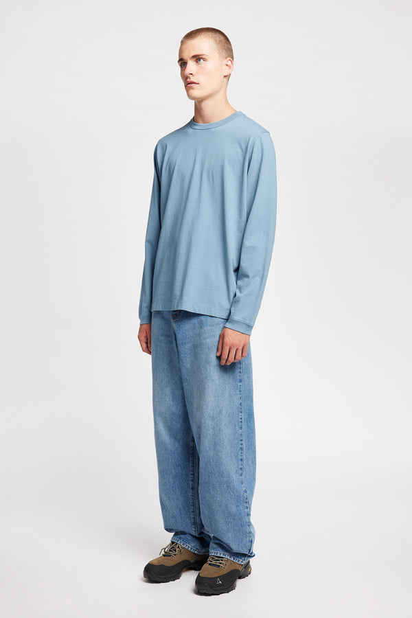 Front view of model in the renew jean, a relaxed loose-fit straight style in premium Japanese denim, shown in mid-blue fade with five-pocket design and custom branded hardware.