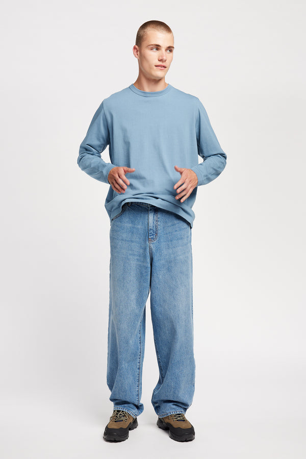 Front view of model in the renew jean, a relaxed loose-fit straight style in premium Japanese denim, shown in mid-blue fade with five-pocket design and custom branded hardware.

