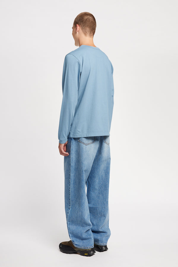 Back view of model in the renew jean, a relaxed loose-fit straight style in premium Japanese denim, shown in mid-blue fade with five-pocket design and custom branded hardware.