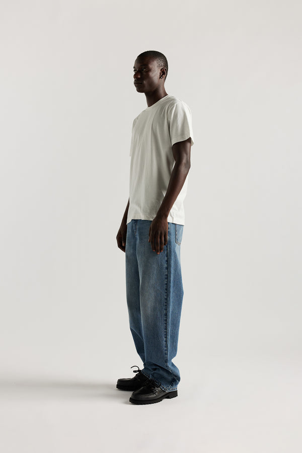 Front view of model in the renew jean, a relaxed loose-fit straight style in premium Japanese denim, shown in mid-blue fade with five-pocket design and custom branded hardware.
