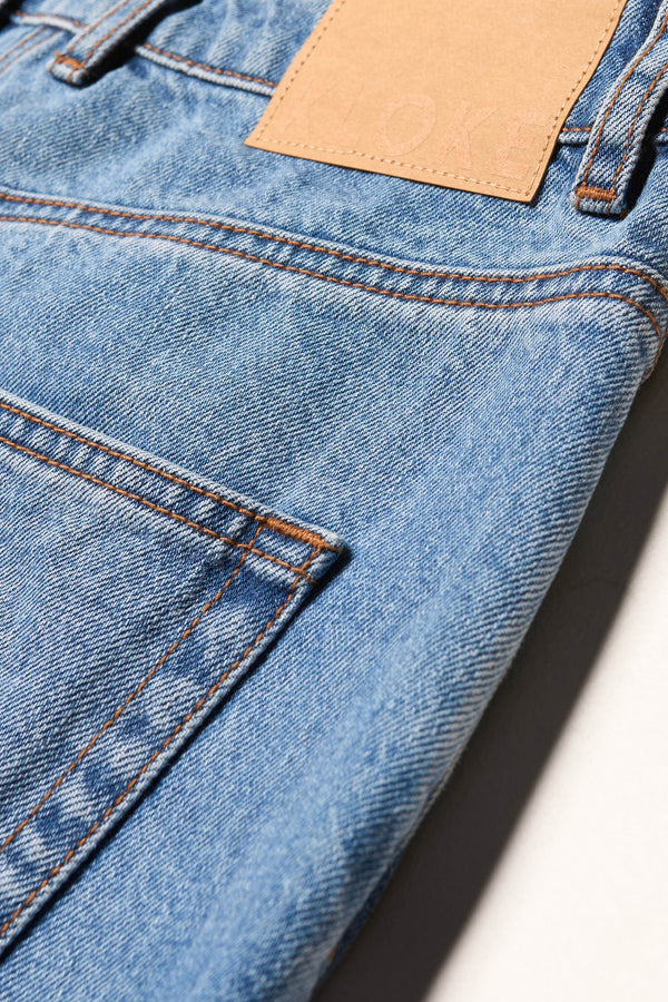 Close up of the renew jean, a relaxed loose-fit straight style in premium Japanese denim, shown in mid-blue fade with five-pocket design and custom branded hardware.
