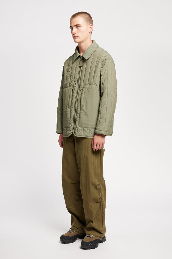 Front angle view of model wearing the response quilted military field jacket with structured collar and concealed zip in dusty olive green
