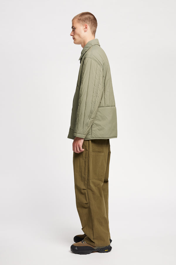 Side view of model wearing the response quilted military field jacket with structured collar and concealed zip in dusty olive green