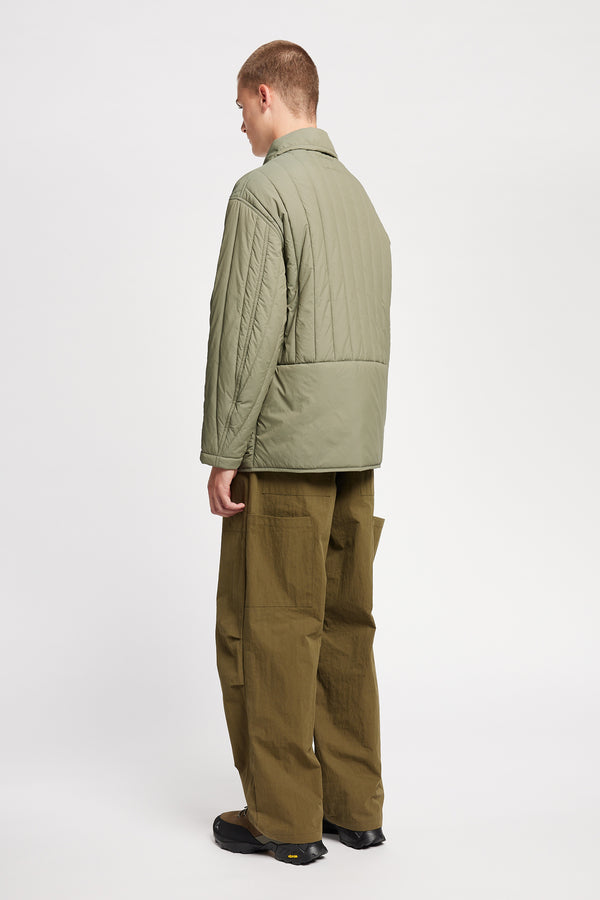 Back angle view of model wearing the response quilted military field jacket with structured collar and concealed zip in dusty olive green