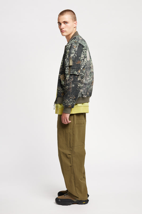 Men Side of Unisex bomber jacket in Green Print woven jacquard with real tree camouflage, featuring dropped shoulders, ribbed trims, and full-length front zip.