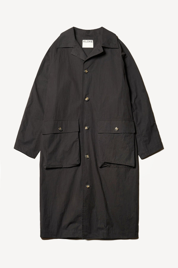 Flat front of the venture trench coat in jet black. An oversized fit in cotton-nylon with structured collar and flap pockets