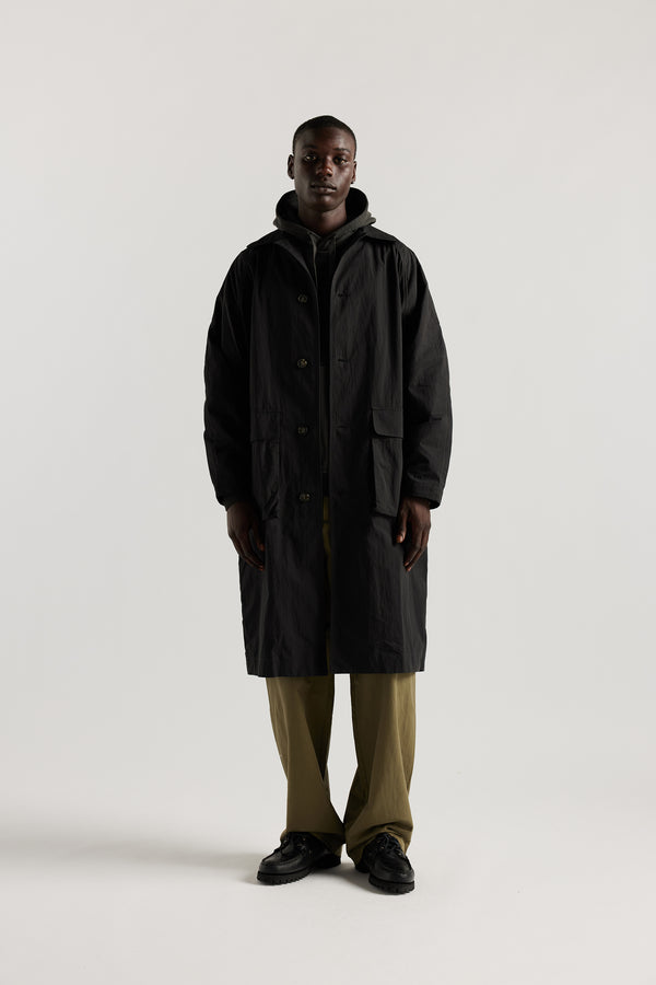 front view of male model wearing the venture trench coat in jet black. An oversized fit in cotton-nylon with structured collar and flap pockets