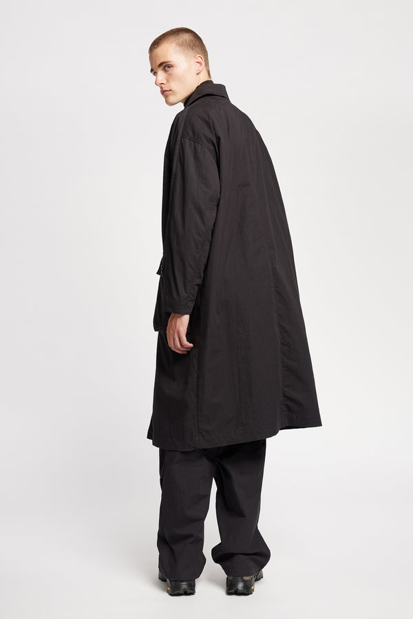 Back view of model wearing the venture trench coat in jet black. An oversized fit in cotton-nylon with structured collar and flap pockets