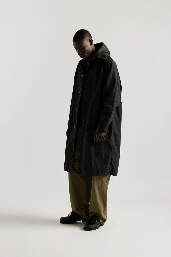 Side front view of male model wearing the venture trench coat in jet black. An oversized fit in cotton-nylon with structured collar and flap pockets