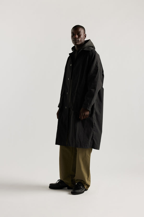 Side front view of male model wearing the venture trench coat in jet black. An oversized fit in cotton-nylon with structured collar and flap pockets
