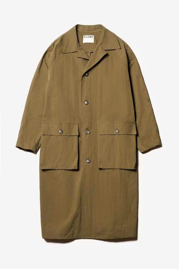 Flat front of the venture trench coat in kelp green. An oversized fit in cotton-nylon with structured collar and flap pockets