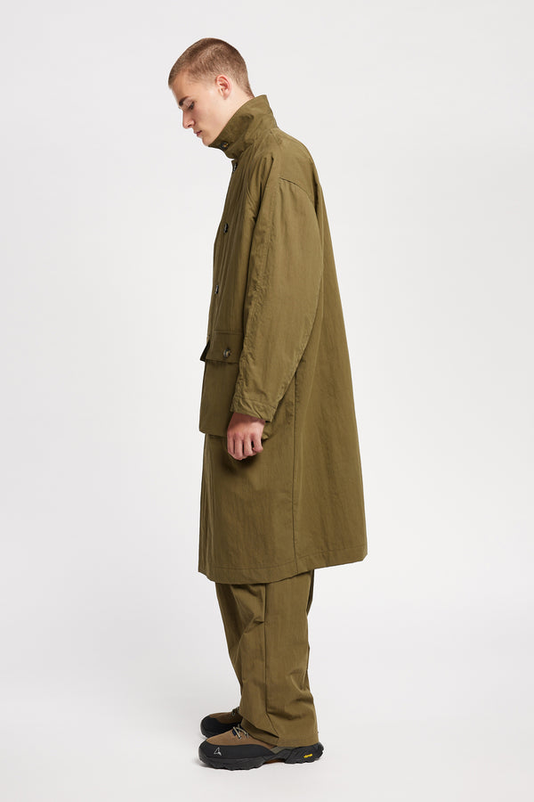 Side view of model wearing the venture trench coat in kelp green. An oversized fit in cotton-nylon with structured collar and flap pockets