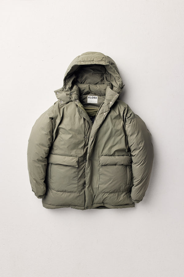 Flat Front of the Men’s Prospect Down Puffa a technical jacket with removable hood and utility pockets, made from recycled nylon. In Dusty Olive Green 