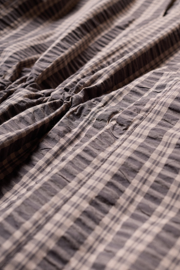 Fabric and details shot of the Origin Dress in gingham seersucker Brown check. A relaxed silhouette with internal tie, clean neckline, and subtle underarm split detail.