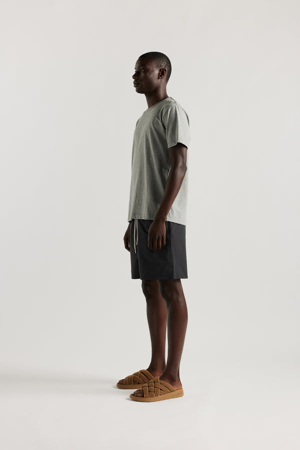 side view of Ousmane wearing relaxed fit swim shorts in black with an elastic drawstring waist and functional pocket detailing.