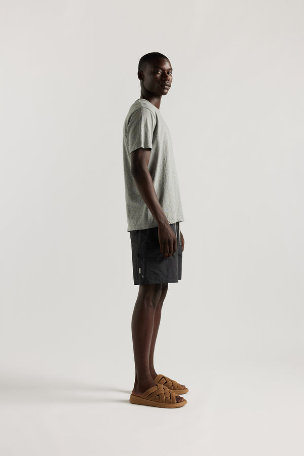 side view of Ousmane wearing relaxed fit swim shorts in black with an elastic drawstring waist and functional pocket detailing.