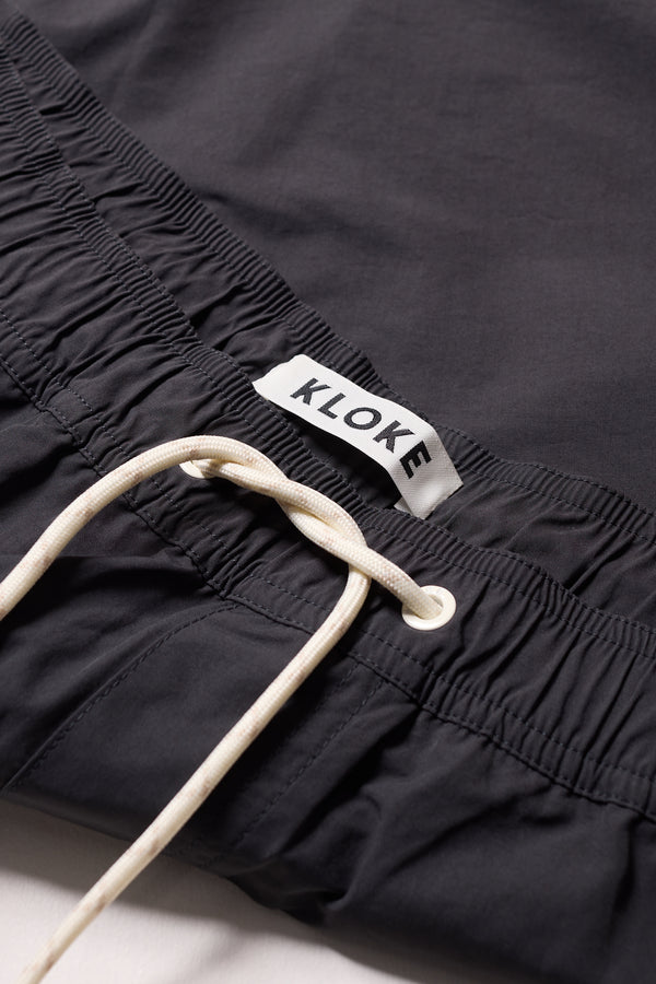 detail shot of relaxed fit swim shorts in black with an elastic drawstring waist and functional pocket detailing.